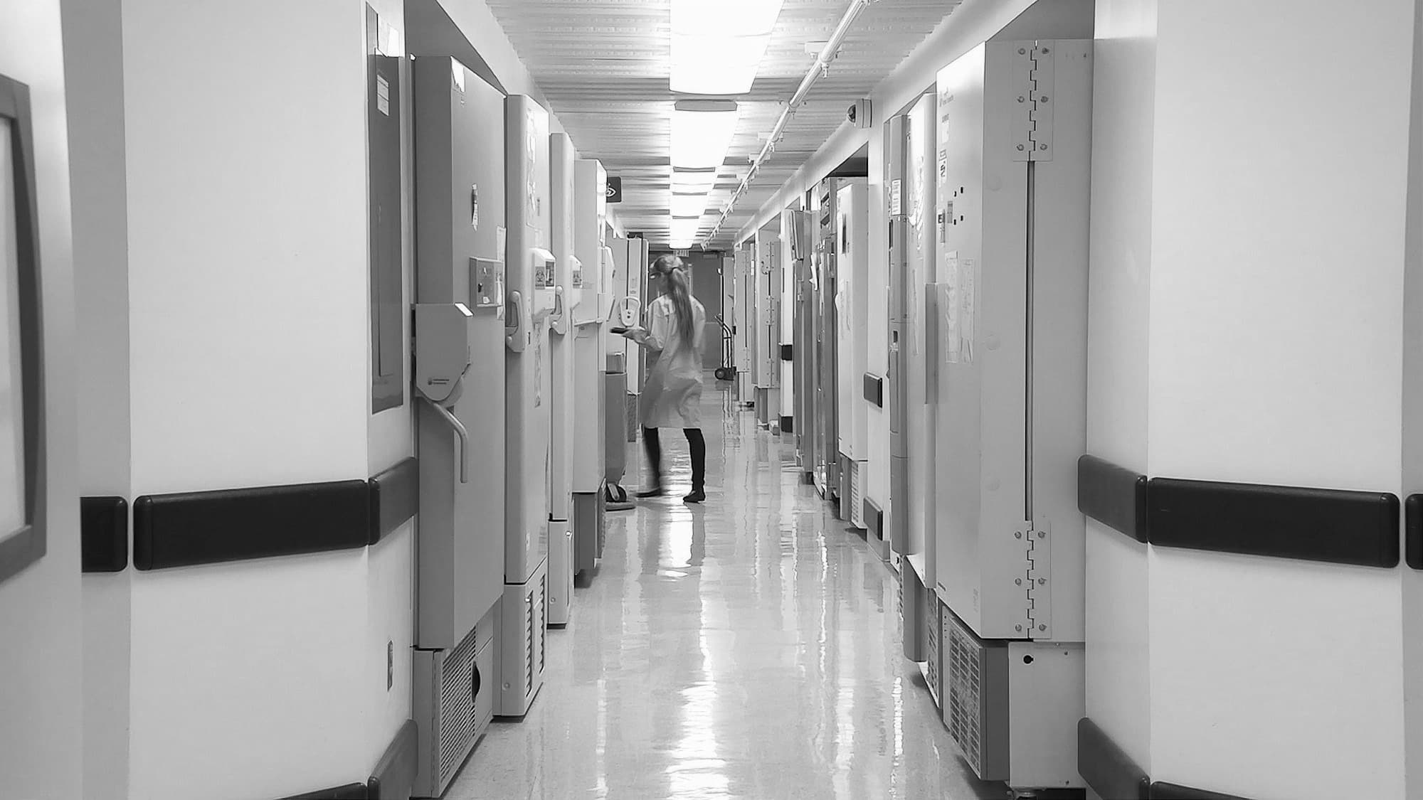 A long clinical corridor lined with equipment, with a person in a lab coat at the far end