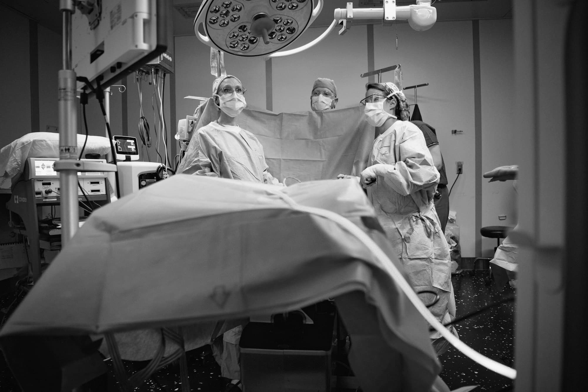 A surgical team in gowns and masks preparing a draped patient under an operating light