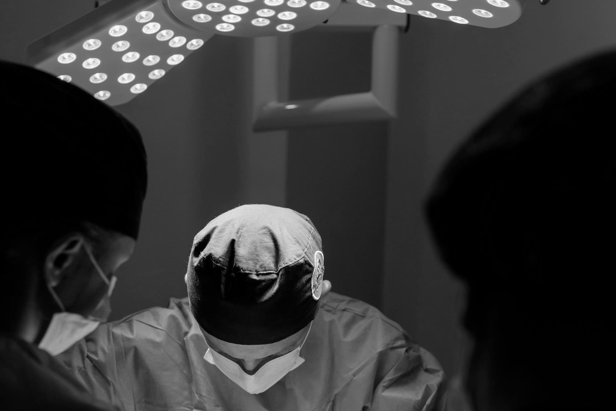 A surgeon in a cap and mask working under operating room lights